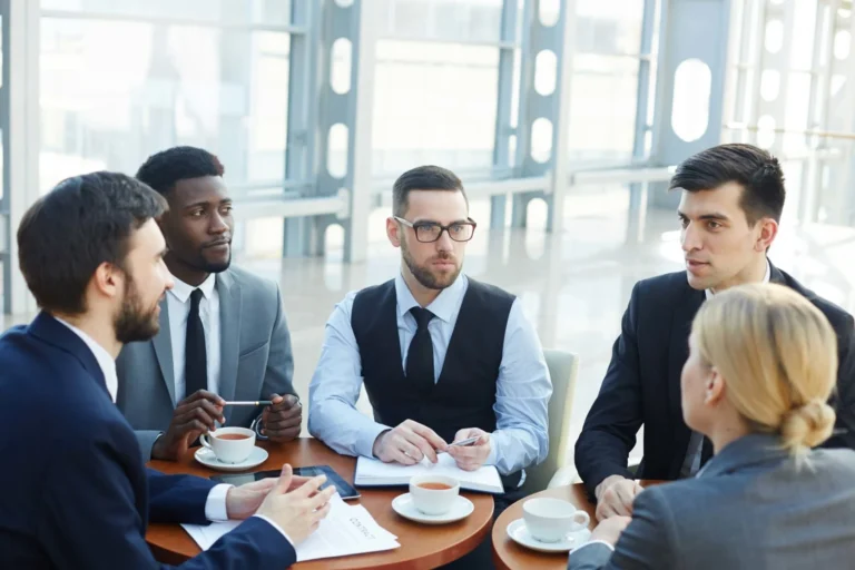 A group of business people gathered around a table discussing contracts while sipping on hot beverages